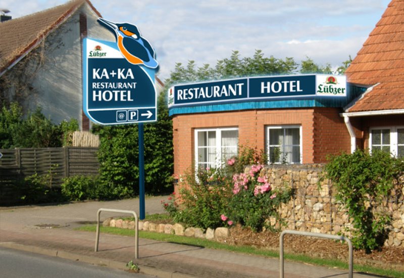 Hinweisschild „KA + KA Restaurant Hotel“ an der Straße, dahinter das Hotelgebäude